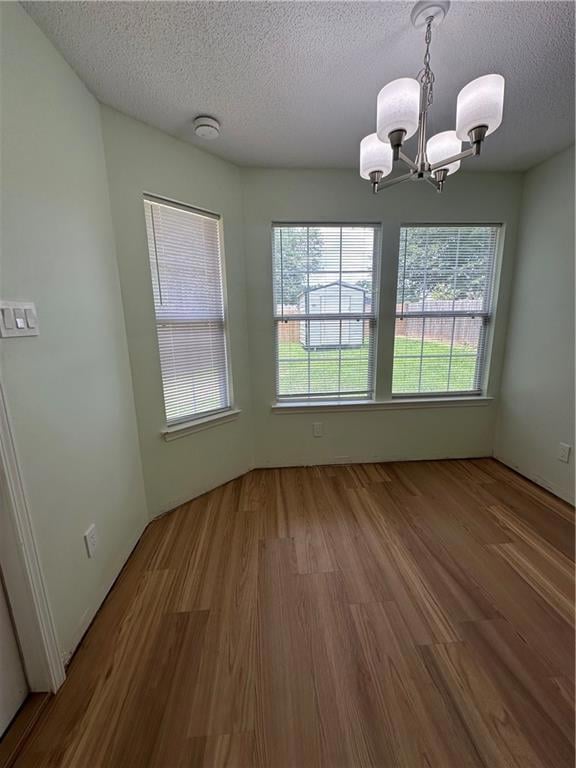 Empty room with a chandelier, wood finished floors, healthy amount of natural light, a textured ceiling, and a smoke detector