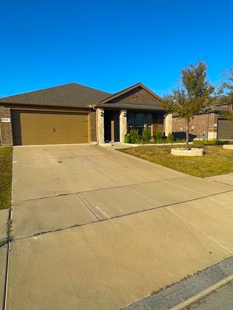 Ranch-style home featuring concrete driveway, brick siding, a garage, a front lawn, and a shingled roof