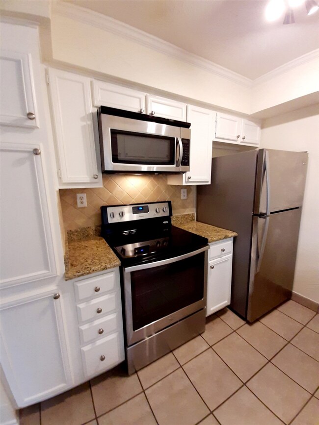 Kitchen with backsplash, appliances with stainless steel finishes, white cabinets, light tile patterned floors, and ornamental molding
