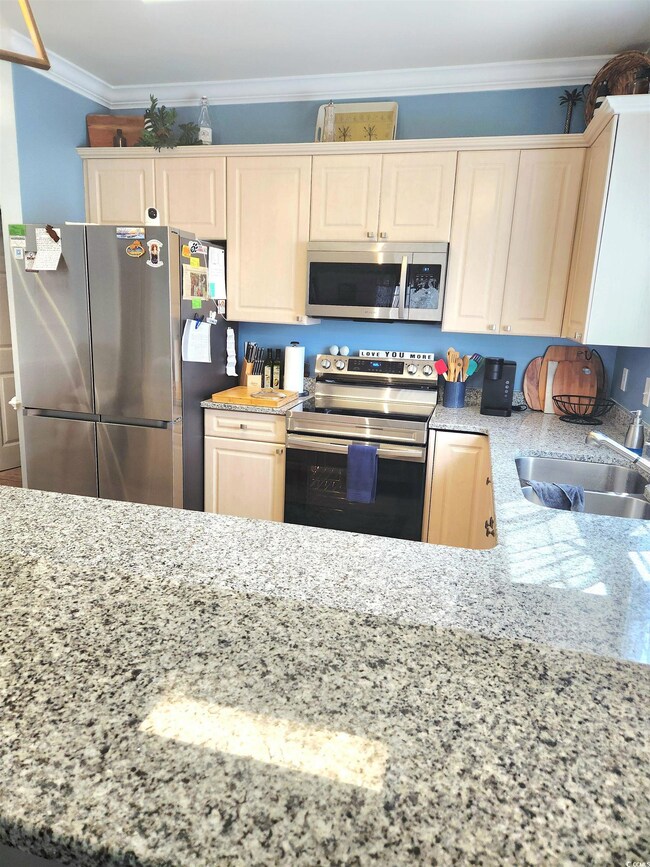 Kitchen with light stone countertops, appliances with stainless steel finishes, and crown molding