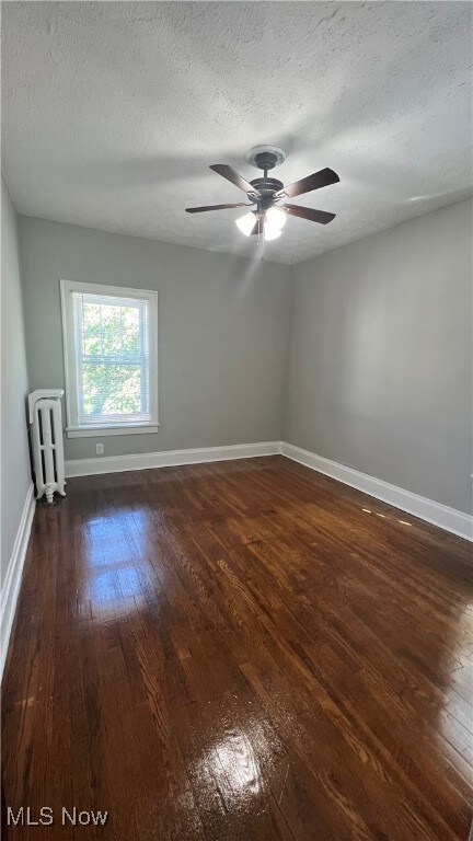 Unfurnished room featuring dark wood finished floors, a textured ceiling, radiator heating unit, and a ceiling fan