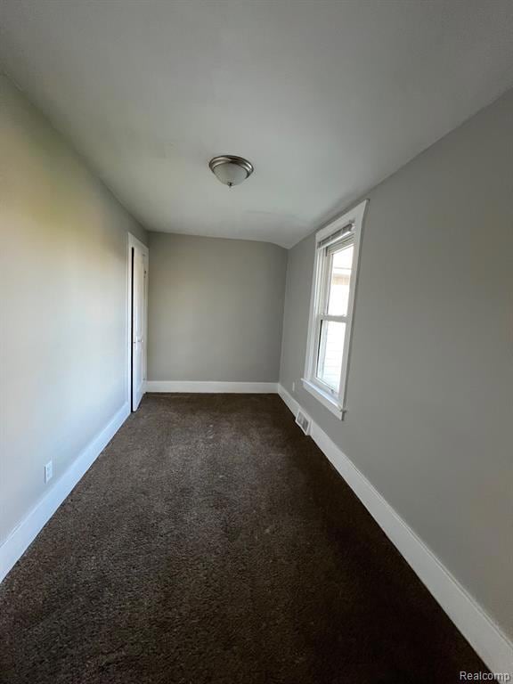 Empty room featuring dark carpet and baseboards