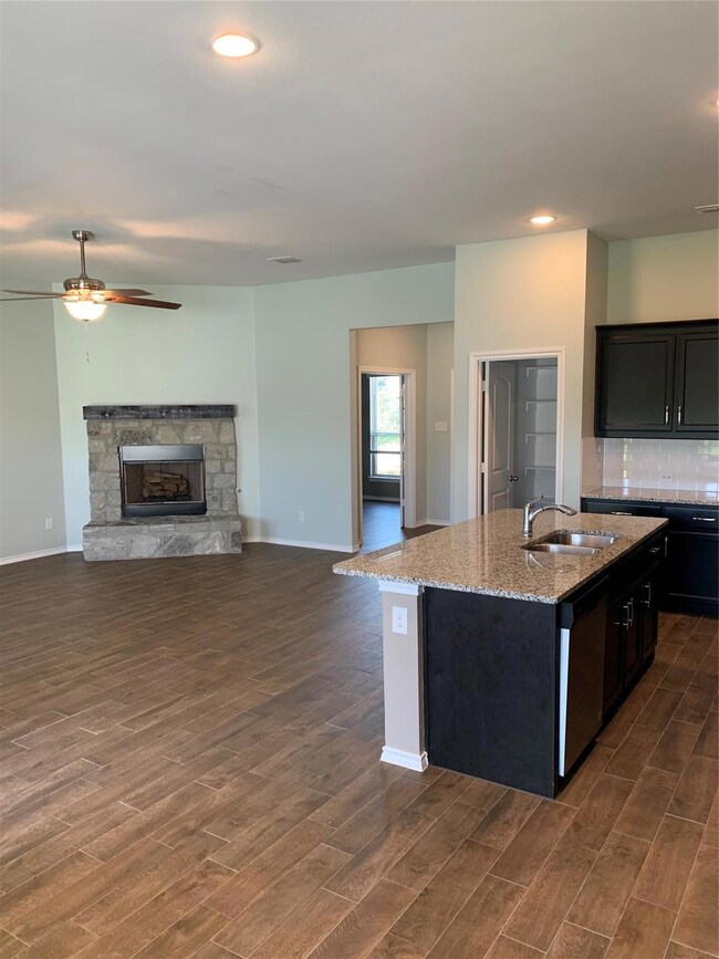 Kitchen featuring a kitchen island with sink, dark hardwood / wood-style flooring, dishwasher, light stone countertops, and a fireplace