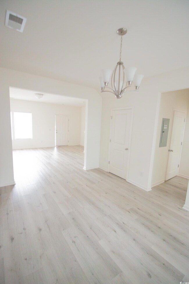 Unfurnished dining area with a chandelier, light wood-style floors, electric panel, and baseboards