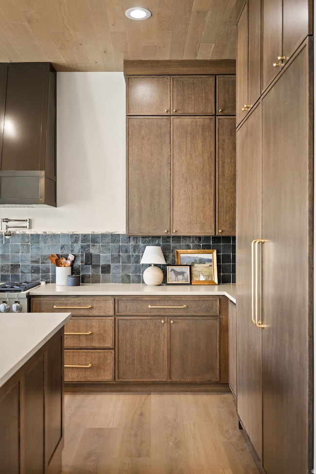 Kitchen featuring paneled built in fridge, light wood-style floors, decorative backsplash, wood ceiling, and recessed lighting