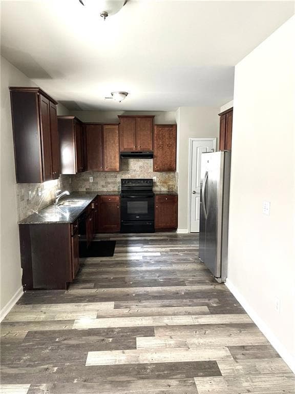 Kitchen with black electric range, stainless steel fridge, decorative backsplash, under cabinet range hood, and wood finished floors