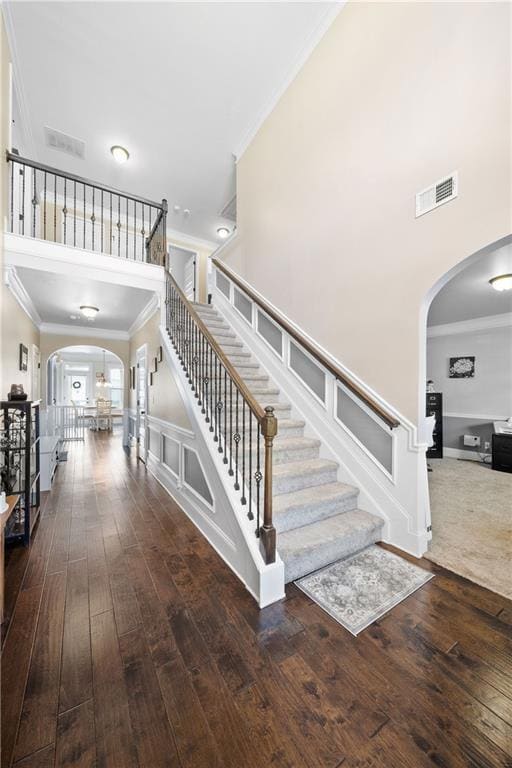 Stairs with arched walkways, crown molding, and wood-type flooring