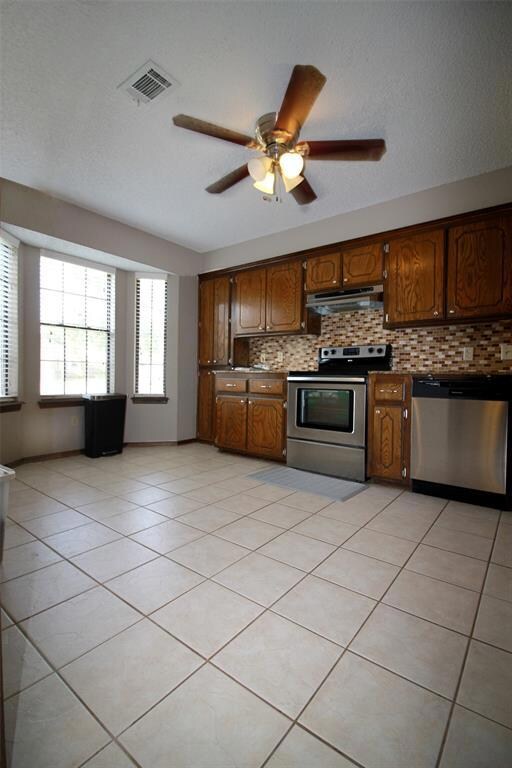 Kitchen featuring light tile patterned floors, backsplash, exhaust hood, ceiling fan, and appliances with stainless steel finishes
