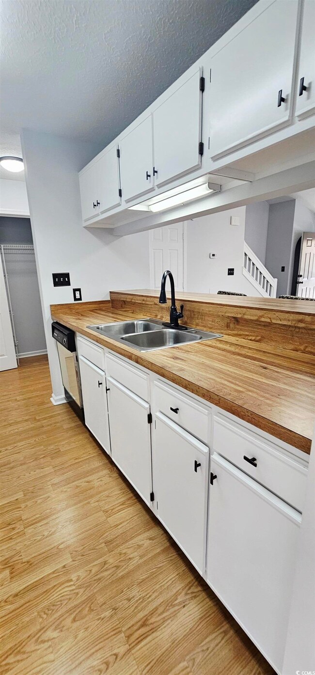 Kitchen with white cabinets, light wood-style floors, wooden counters, and a textured ceiling