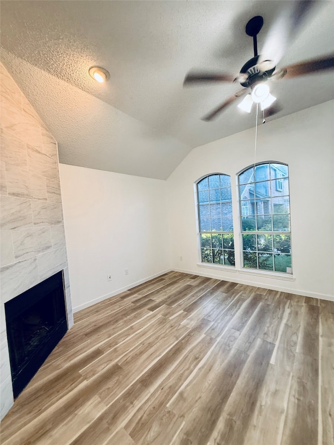 Unfurnished living room featuring a textured ceiling, lofted ceiling, light wood-style flooring, a tiled fireplace, and a ceiling fan