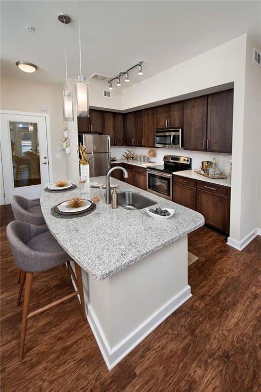 Kitchen with appliances with stainless steel finishes, a kitchen bar, sink, and dark wood-type flooring