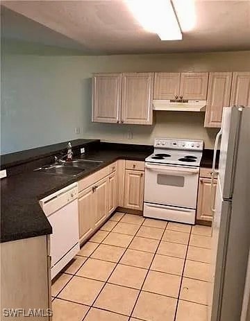 Kitchen with dark countertops, a sink, white appli