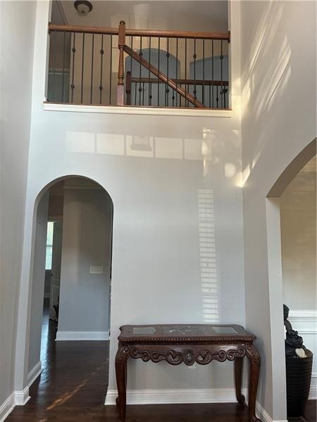 Hall with arched walkways, dark wood-style flooring, and a high ceiling