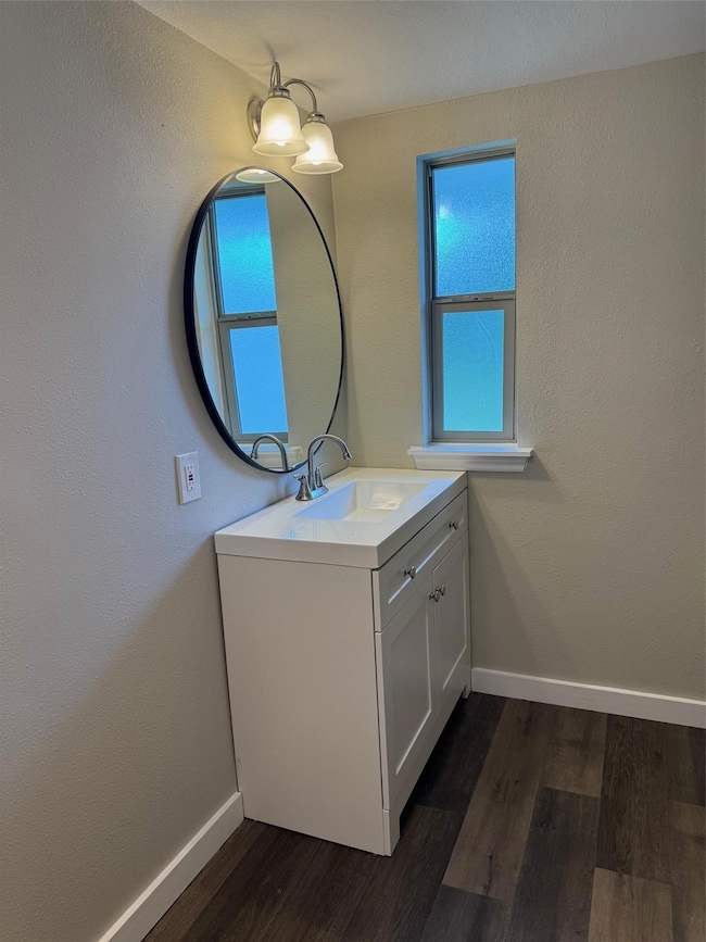 Half bath with a textured wall, dark wood-type flooring, and vanity
