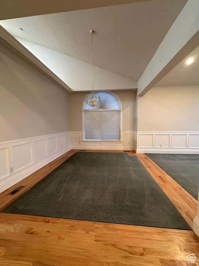 Unfurnished dining area featuring wainscoting, a decorative wall, lofted ceiling, and wood finished floors
