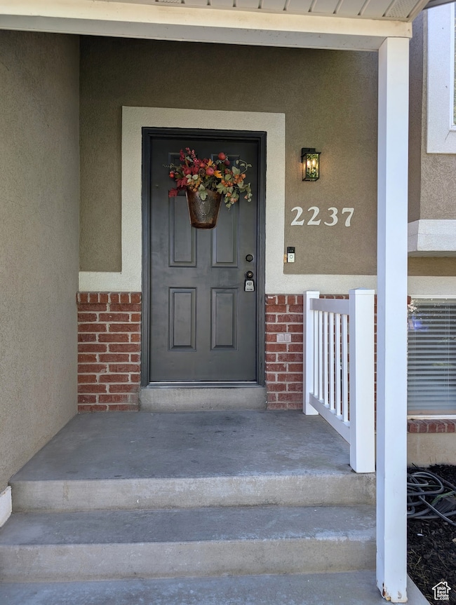 Property entrance featuring a porch, brick siding, and stucco siding