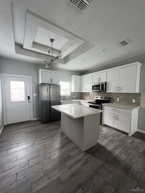 Kitchen with dark hardwood / wood-style flooring, white cabinets, a healthy amount of sunlight, and stainless steel appliances