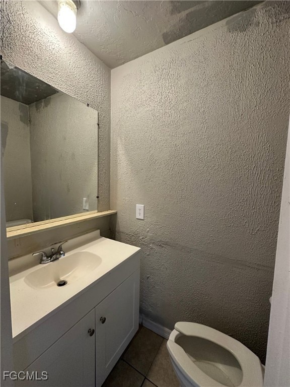 Half bathroom featuring a textured wall, dark tile patterned floors, and vanity