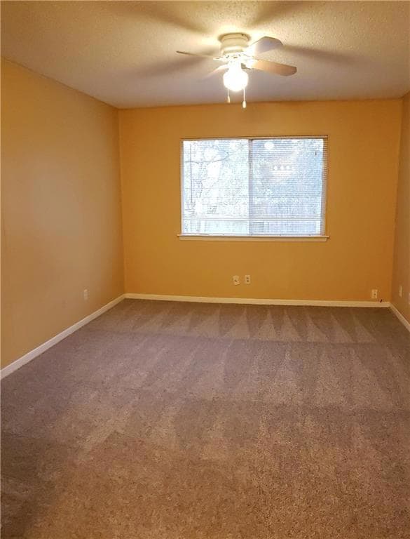 Carpeted empty room with a ceiling fan and basebo