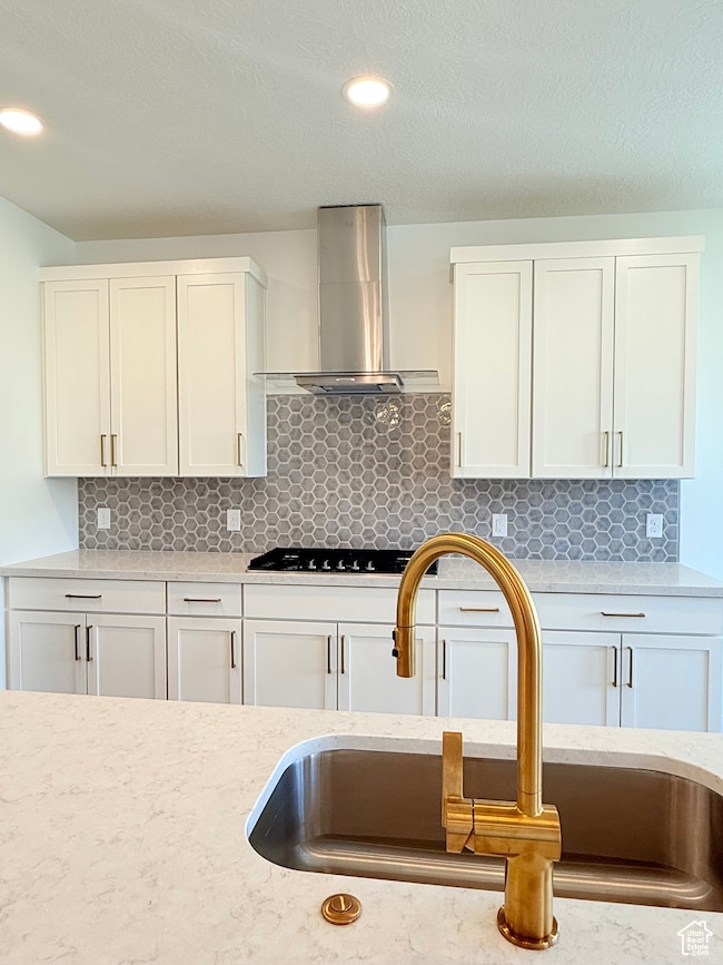 Kitchen featuring light stone counters, white cabinetry, tasteful backsplash, wall chimney exhaust hood, and a textured ceiling