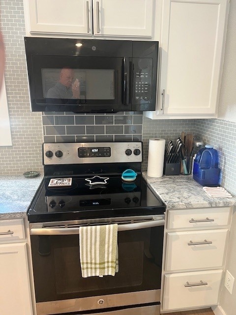 Kitchen with black microwave, decorative backsplash, electric stove, and white cabinets