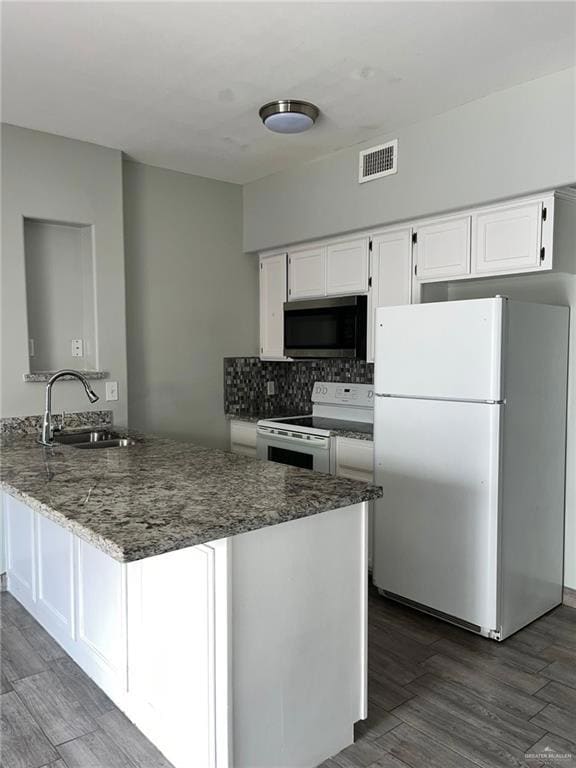 Kitchen featuring white appliances, white cabinets, a peninsula, decorative backsplash, and dark stone counters