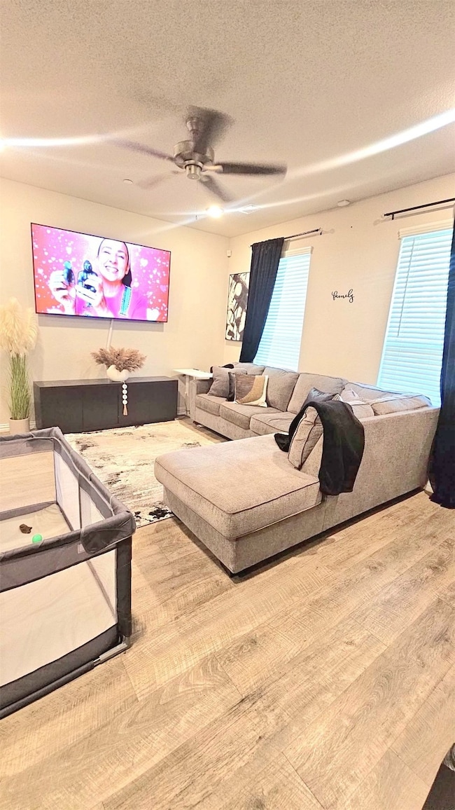 Living area featuring a textured ceiling, wood finished floors, ceiling fan, and plenty of natural light