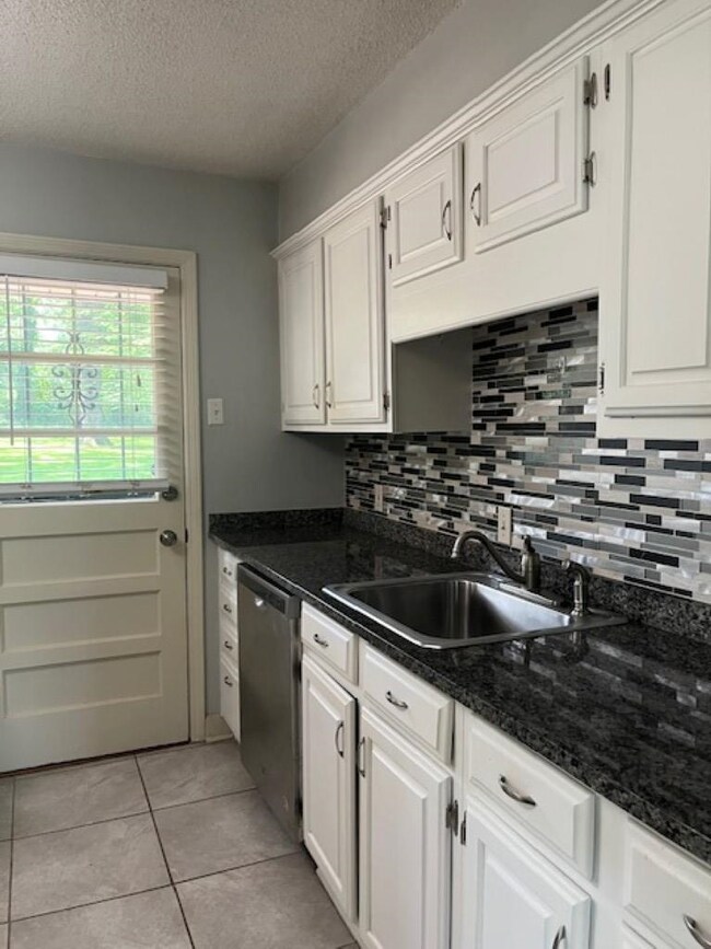 Kitchen with a sink, dishwasher, white cabinetry, decorative backsplash, and a textured ceiling