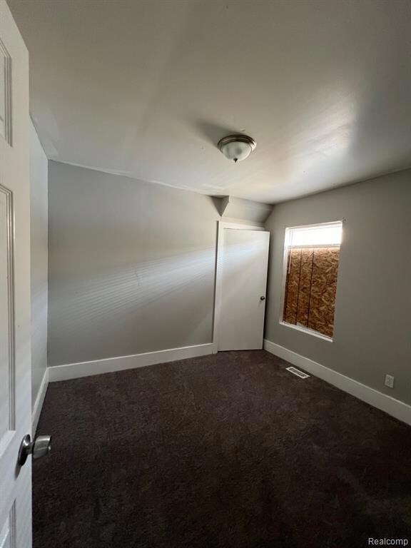 Spare room featuring dark carpet and baseboards