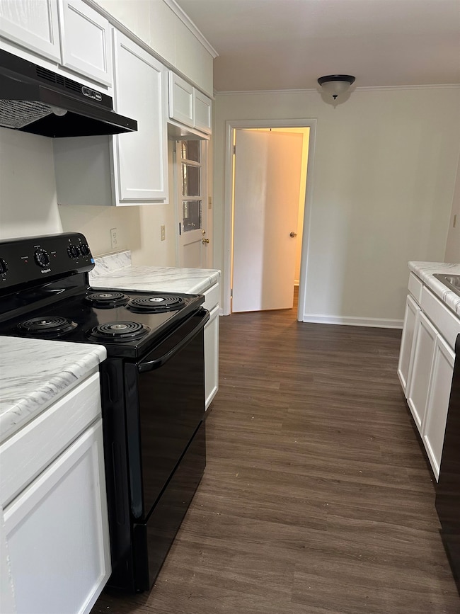 Kitchen with black range with electric stovetop, under cabinet range hood, white cabinets, dark wood-type flooring, and ornamental molding