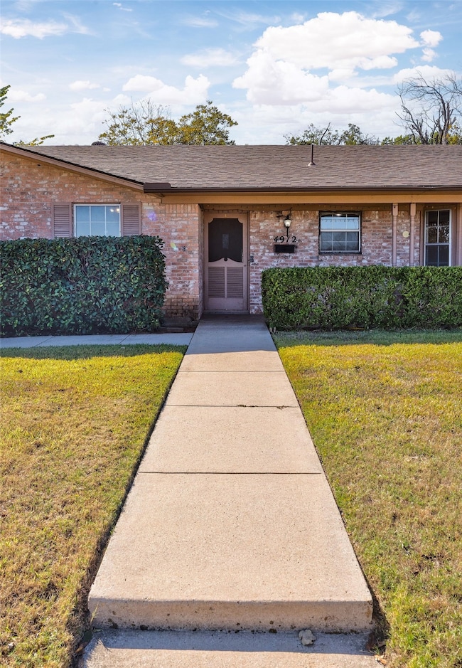View of front of home with a front lawn, brick siding, and a shingled roof