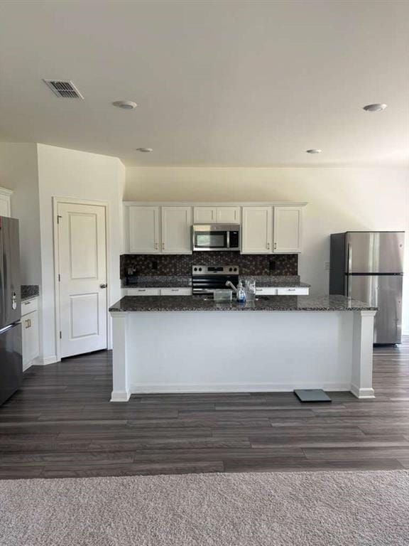 Kitchen with decorative backsplash, white cabinetry, appliances with stainless steel finishes, an island with sink, and dark stone counters