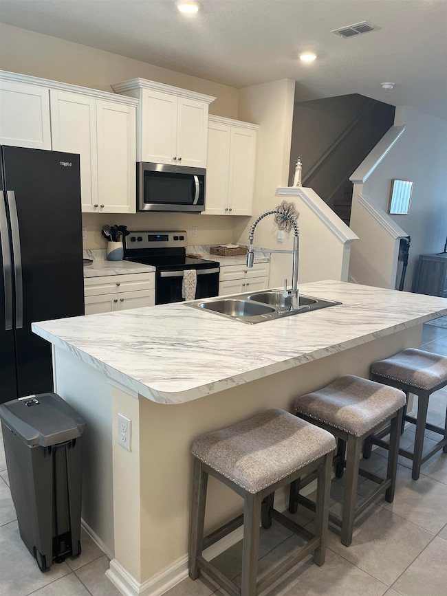 Kitchen with light tile patterned floors, a kitchen breakfast bar, stainless steel appliances, light countertops, and recessed lighting