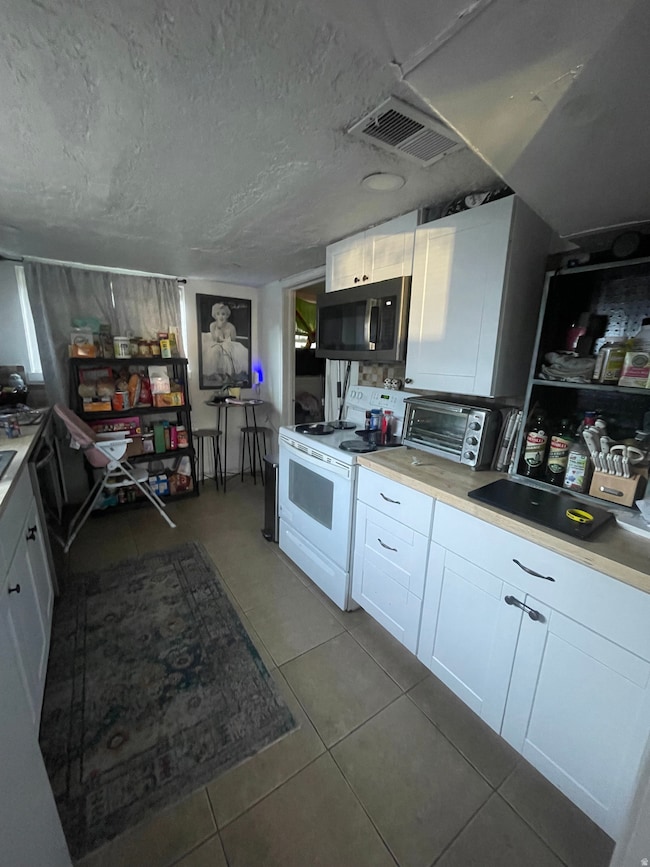 Kitchen featuring white cabinets, a textured ceiling, white electric range oven, light countertops, and light tile patterned floors