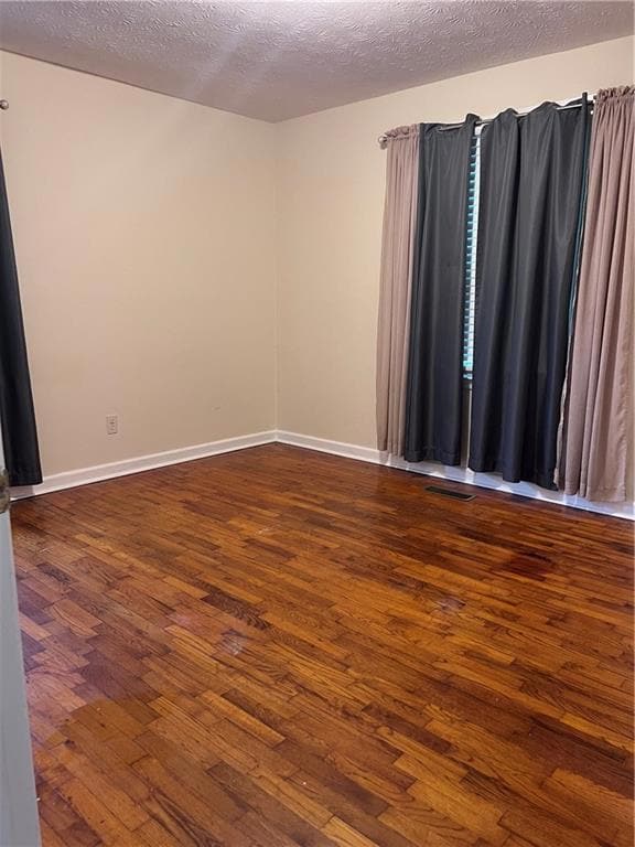 Spare room featuring dark wood finished floors, a textured ceiling, and baseboards