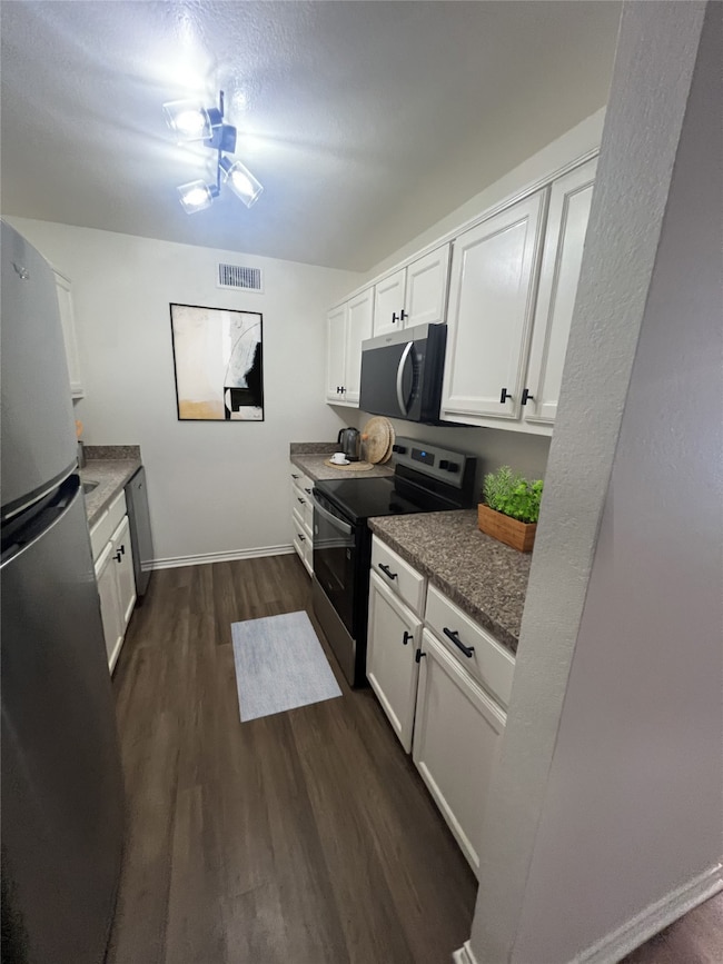 Kitchen with appliances with stainless steel finishes, dark wood-style floors, white cabinetry, a textured ceiling, and dark countertops