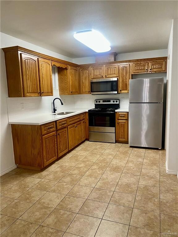Kitchen featuring brown cabinets, a sink, tasteful backsplash, stainless steel appliances, and light countertops