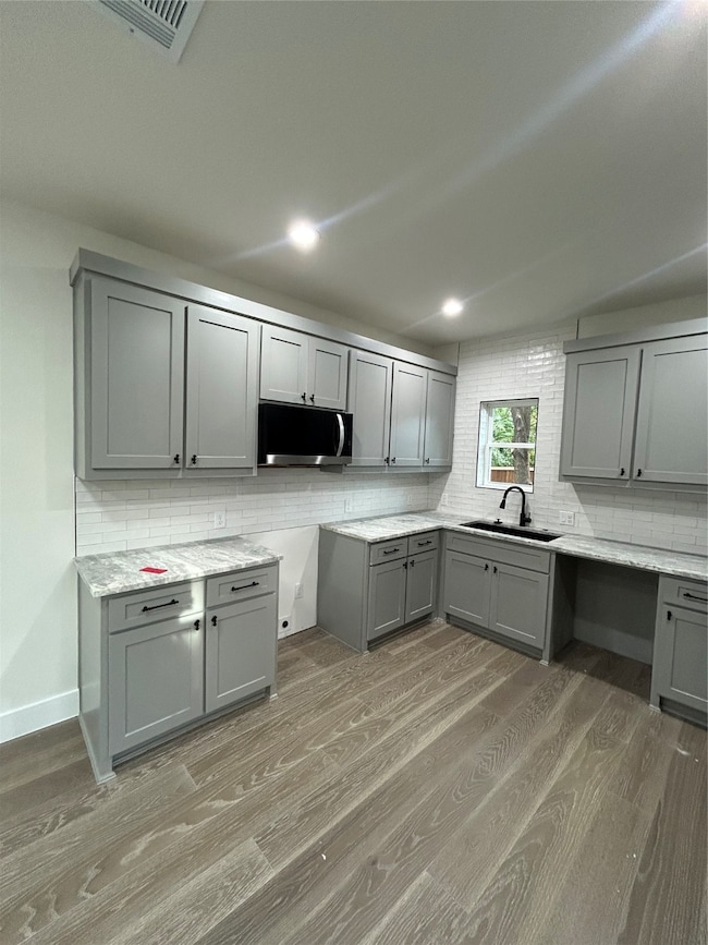 Kitchen with gray cabinets, decorative backsplash, light wood finished floors, recessed lighting, and light stone countertops