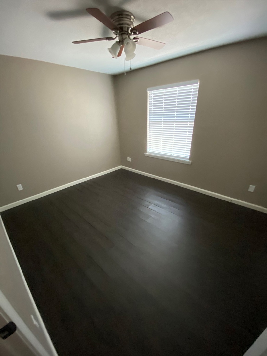 Empty room with dark wood-type flooring, baseboards, and ceiling fan