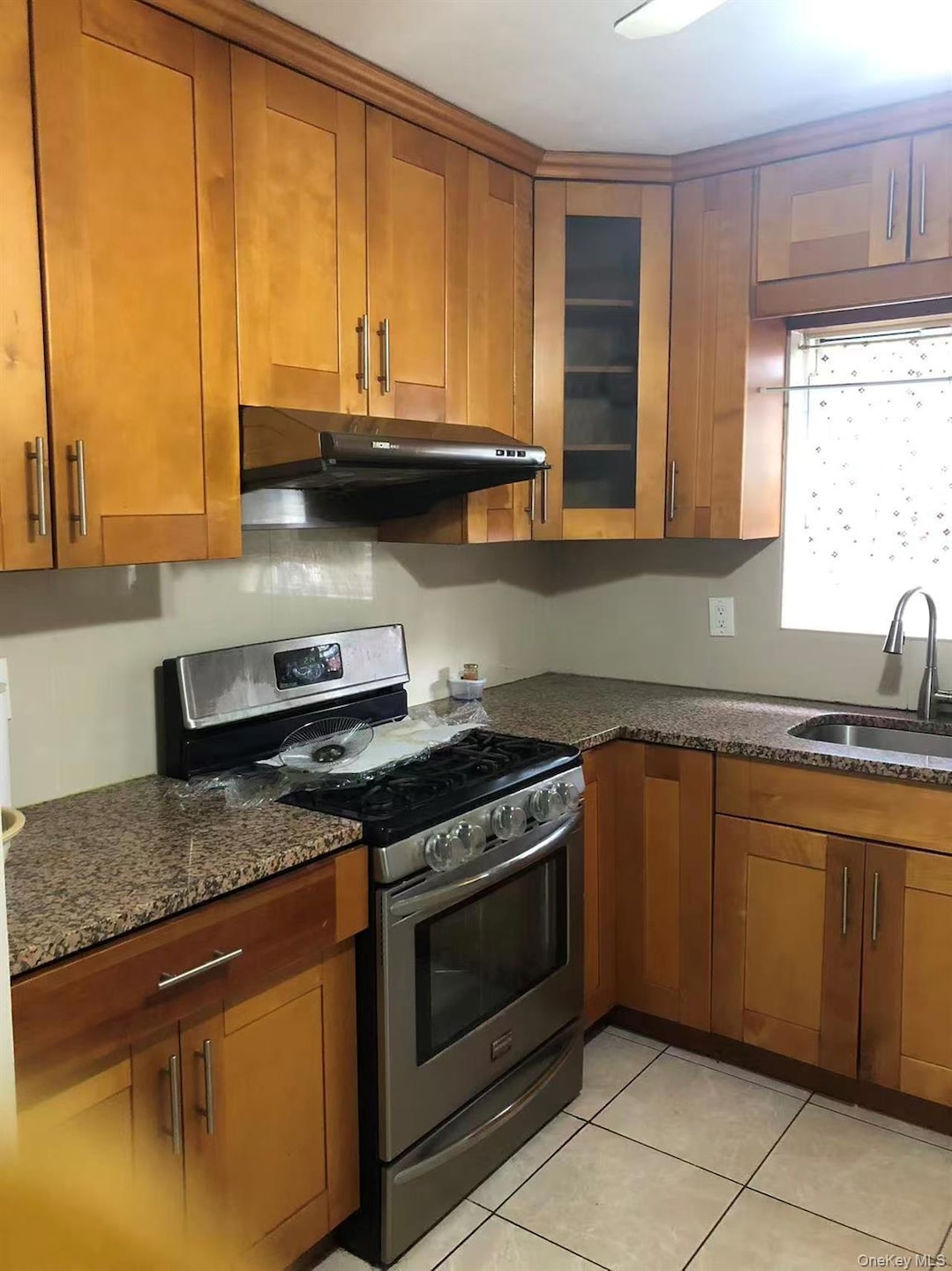 Kitchen featuring gas range, brown cabinets, under cabinet range hood, dark stone counters, and light tile patterned flooring