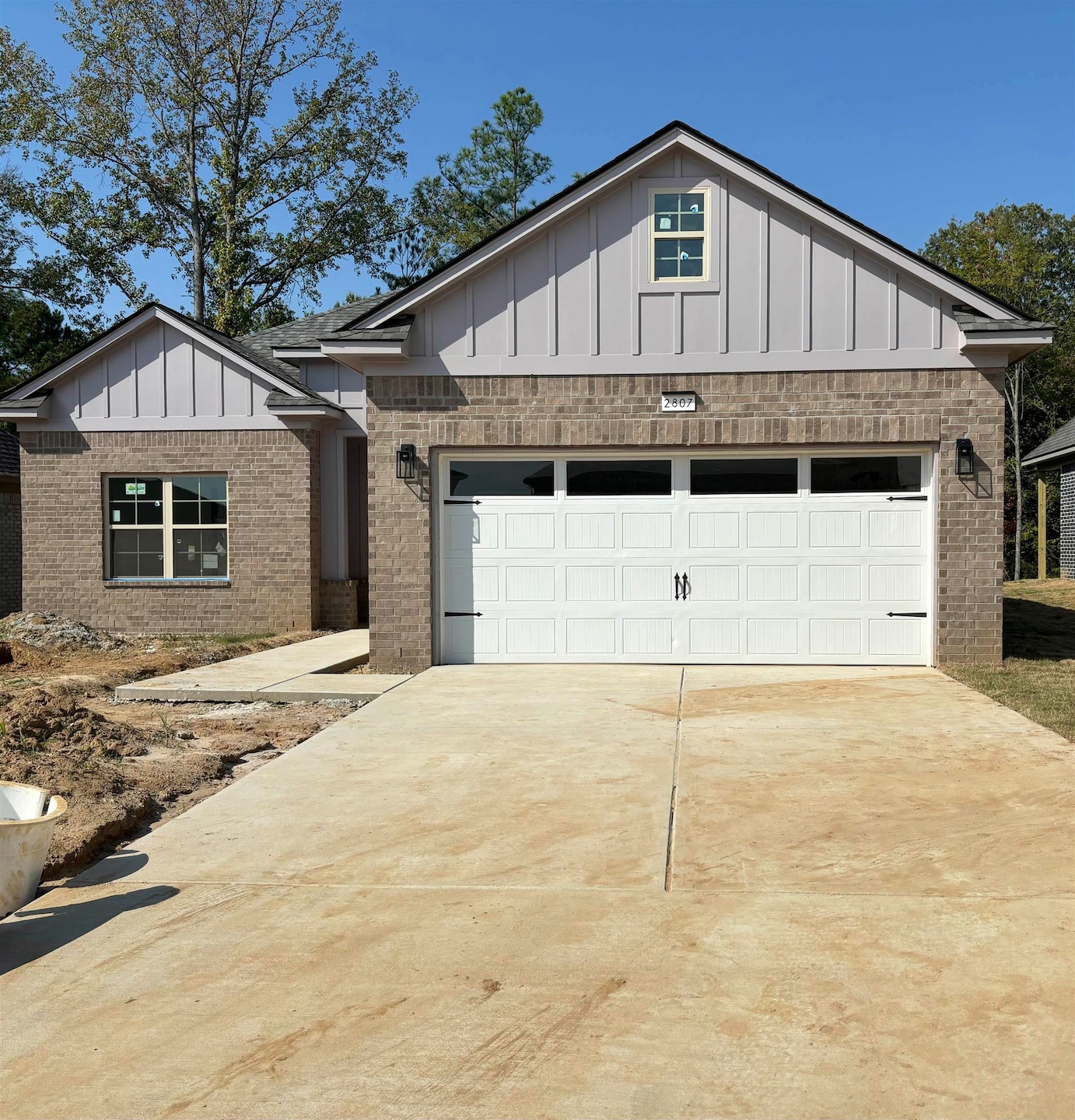 View of front of property with board and batten siding, driveway, brick siding, and an attached garage