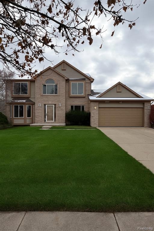 Traditional home featuring a front lawn, brick siding, and driveway