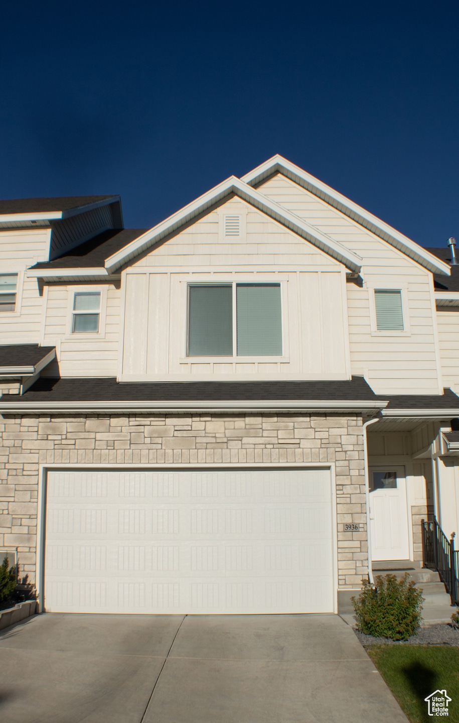 View of front of home featuring a garage, concrete driveway, stone siding, and board and batten siding