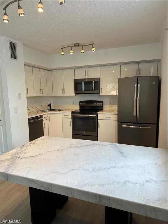 Kitchen featuring black appliances, light stone counters, white cabinets, and a textured ceiling
