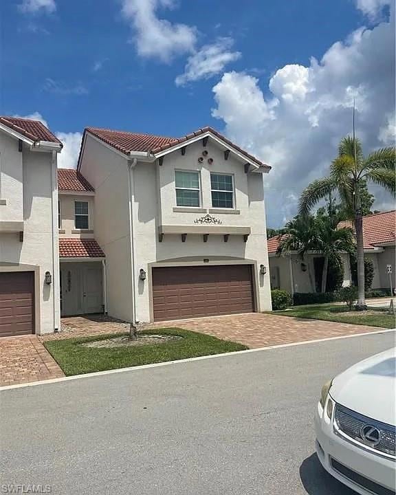 Mediterranean / spanish home with decorative driveway, stucco siding, a tile roof, and an attached garage
