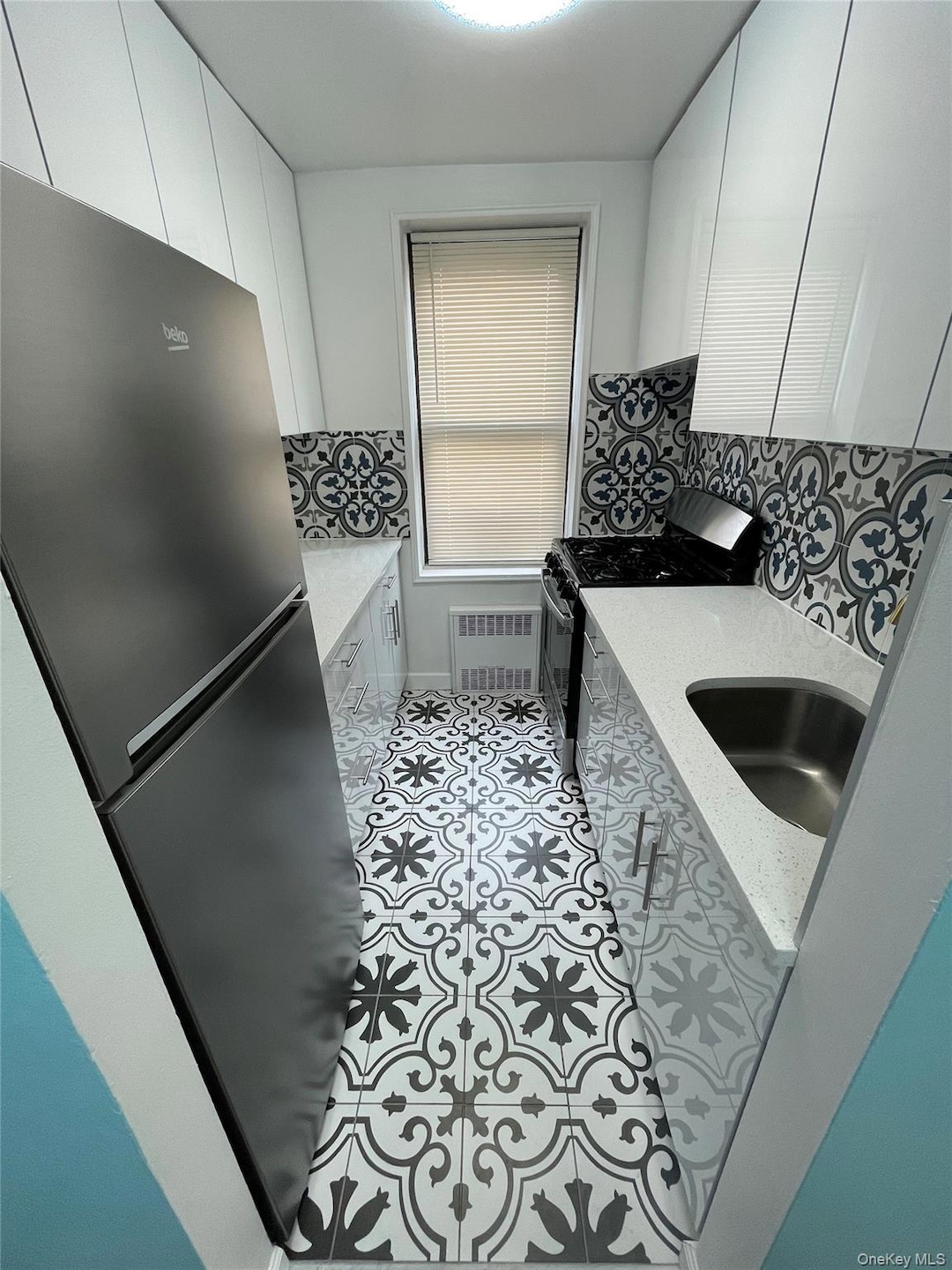 Kitchen featuring stainless steel appliances, white cabinetry, radiator, tile patterned flooring, and light stone counters