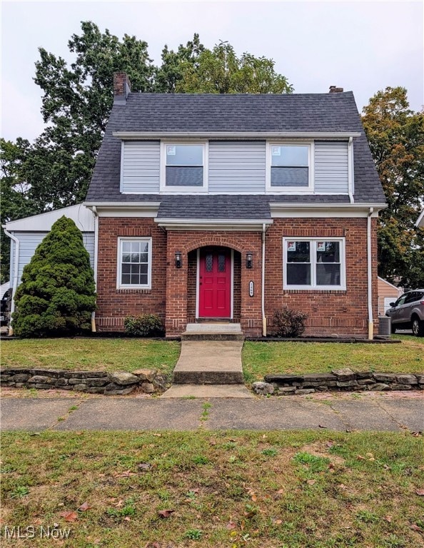 View of front of property featuring a chimney, brick siding, and a front yard