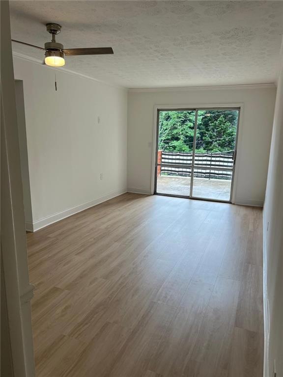 Spare room with crown molding, light wood-type flooring, a ceiling fan, baseboards, and a textured ceiling