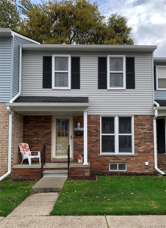 Traditional home with covered porch, a front yard, and brick siding