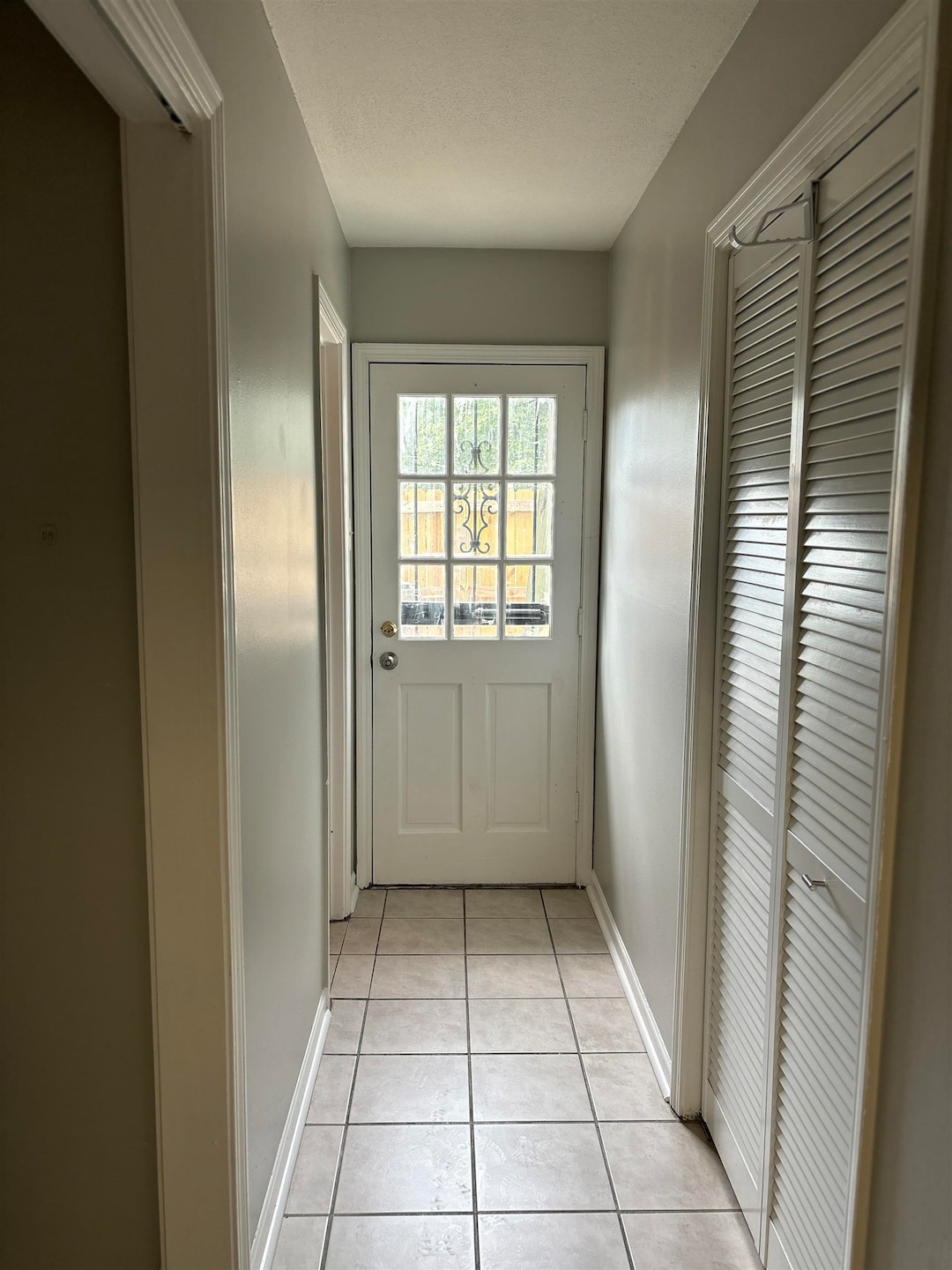 Doorway with light tile patterned floors, baseboards, and a textured ceiling